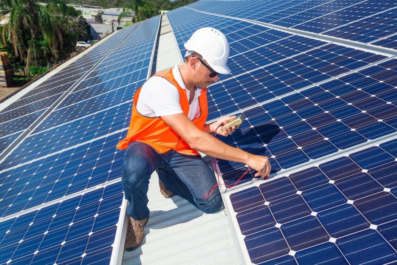 A man in an orange vest and hard hat working on solar panels.